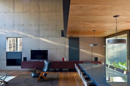 ampla sala com painel de concreto aparente com mesa de vidro bem comprida e cadeira de couro preta