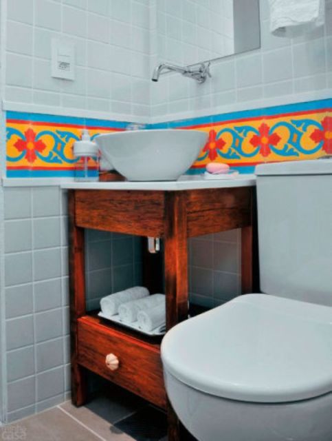 banheiro com louças e azulejos nas paredes brancos e faixa de azulejos em tons de amarelo, azul e vermelho