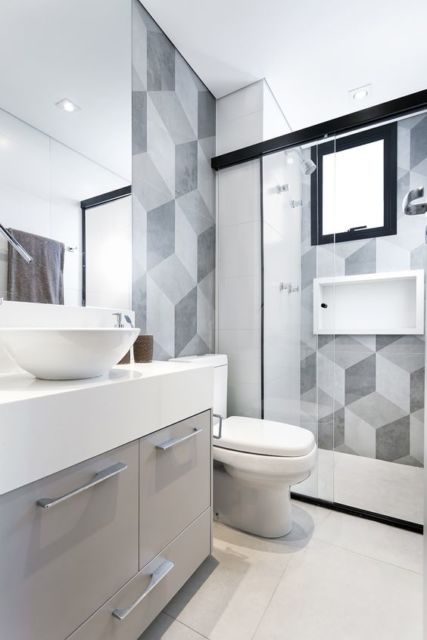 banheiro com louças brancas, box de vidro e faixa de azulejos com desenho geométrico formando vários cubos em tons de cinza