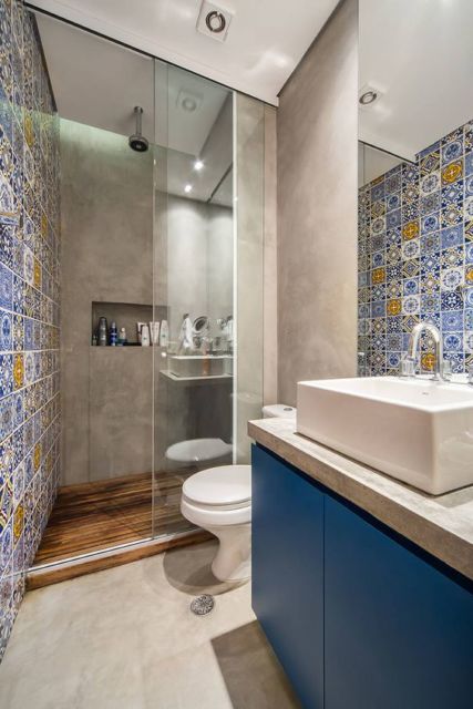Banheiro com parede de ladrilho hidráulico, box de vidro, louças brancas e piso de azulejo off white