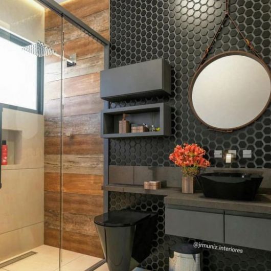 Banheiro com louças pretas, parede de desenhos geométricos de fórmica e parede de azulejo imitando madeira dentro do box