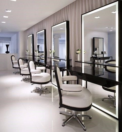 salão com cadeiras brancas de molde preto e grandes espelhos revestidos de luz de LED