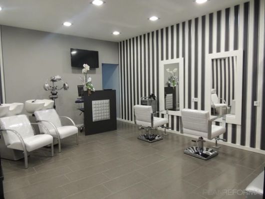 Ambiente de salão de beleza com piso e uma parede cinzas, outra parede com papel de parede listrado em preto e branco