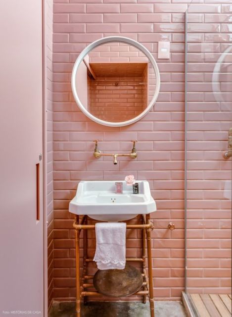banheiro com azulejos e porta rosas, e espelho redondo