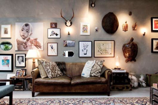 sala com sofá de couro e parede decorada com diversos quadros e esculturas