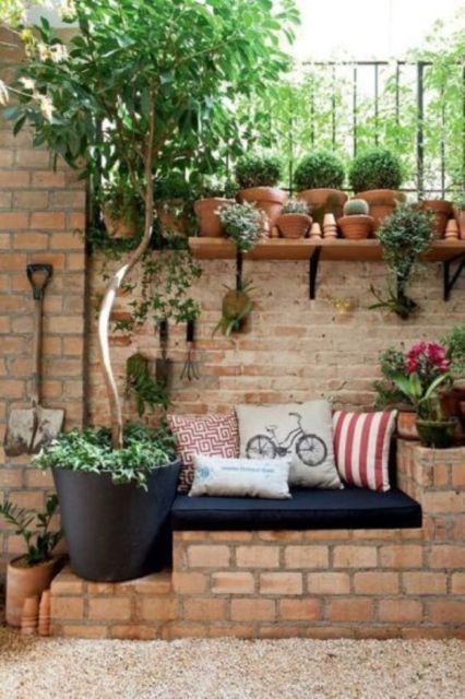 parede de tijolinhos com diversos vasos de plantas e um banco embutido com almofada preta