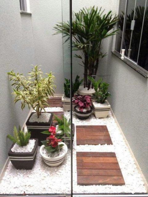 Jardim interno com chão recoberto de pedrinhas brancas e vasos de plantas com porta de vidro