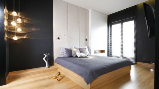 quarto de casal com piso e cama de madeira, paredes pretas e cabeceira branca