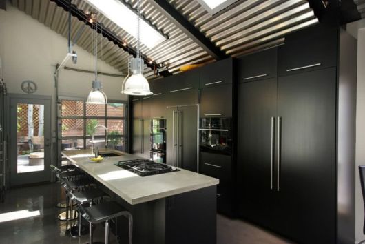 cozinha com ilha com balcão branco, armários e eletrodomésticos pretos