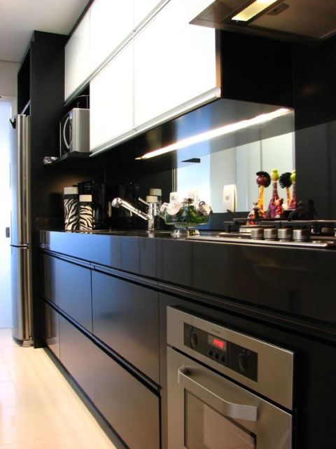 cozinha com armários superiores brancos e inferiores pretos, fogão de placa e forno embutido cromado