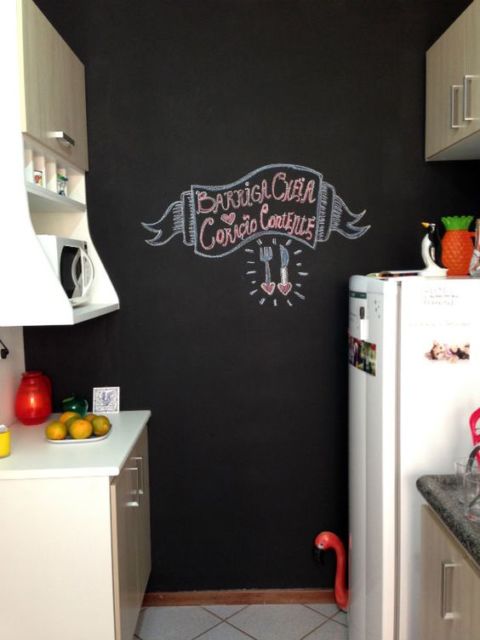 cozinha com parede de lousa com escritos "barriga cheira coração contente", eletrodomésticos e armários brancos
