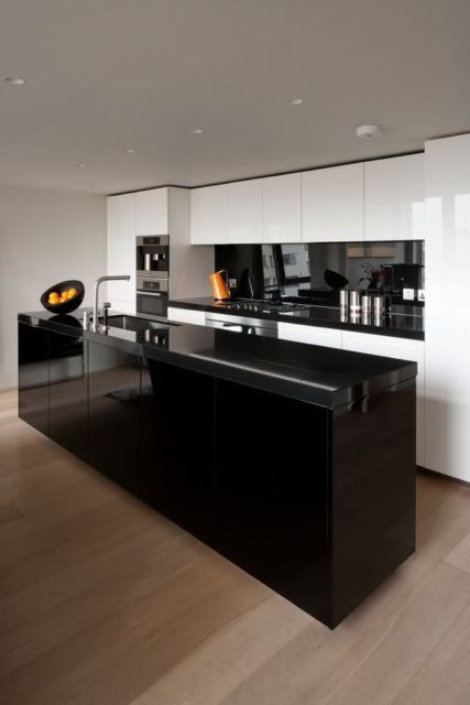 cozinha com armários planejados brancos, ilha preta com leve brilho e piso de madeira