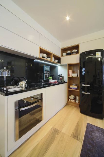 cozinha com armários brancos, geladeira preta, parede preta sobre a pia e piso de madeira em tom claro