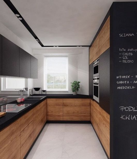 Cozinha com armários inferiores em tom de madeira, superiores pretos, teto branco com faixa preta e parede de lousa no primeiro plano