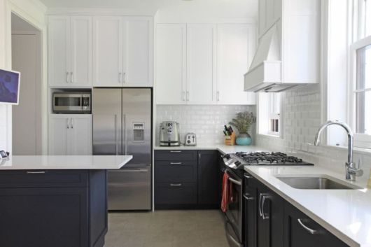 cozinha com eletrodomésticos cromados, armários brancos em cima e pretos embaixo