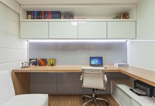 escritório em casa planejado, cadeira giratória branca, bancada que ocupa duas paredes em madeira em tom claro