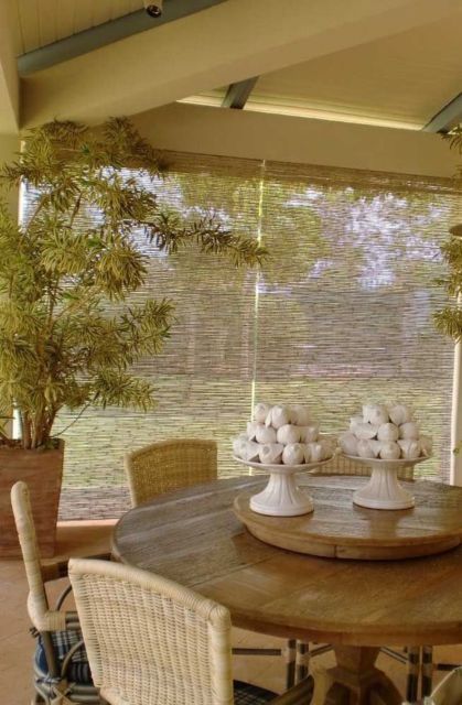 sala com mesa redonda de madeiras, cadeiras com encosto de vime e grandes cortinas de bambu de textura fina