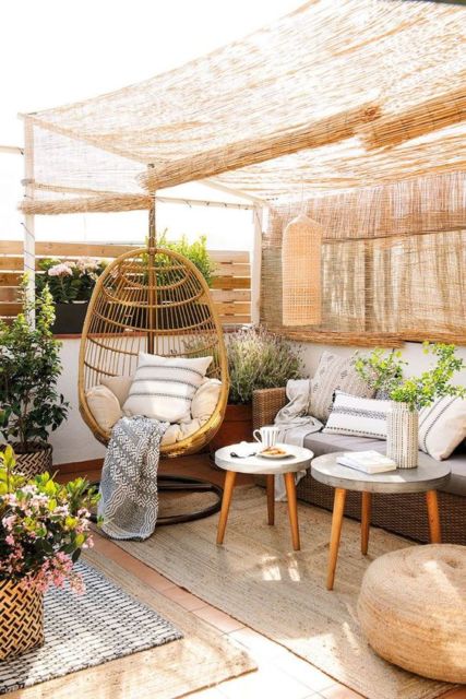 varanda com mesinhas redondas, uma poltrona com encosto alto e cortinas de bambu no teto