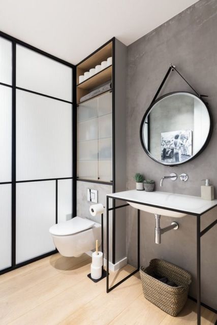 banheiro com vaso sanitário branco, espelho redondo, pia branca suspensa por pés de metal preto