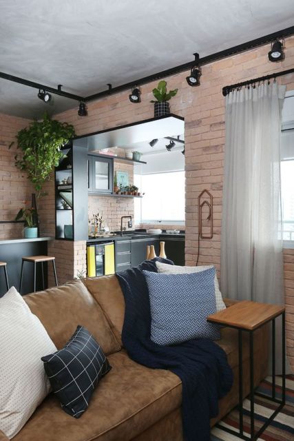 sala com paredes de tijolinhos à mostra, sofá marrom com almofadas branca, preta e azul