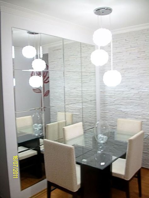 sala de jantar com espelho grande, mesa de vidro com quatro cadeiras brancas e lustre com três bolas brancas