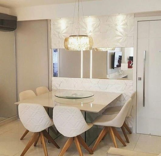 mesa branca com seis cadeiras brancas, espelho e lustre parcialmente transparente