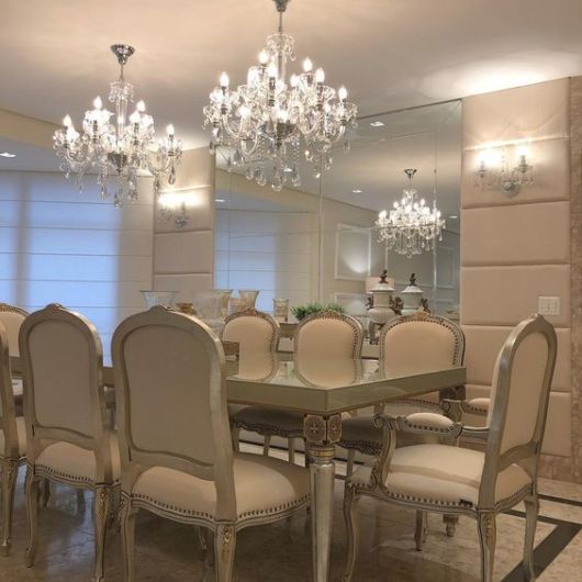 sala de jantar cm grande espelho, dois lustres de cristal pendentes do teto, mesa de jantar de madeira com oito cadeiras