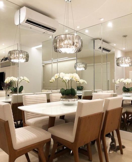 sala de jantar com paredes de espelho, mesa com seis cadeiras brancas e lustre pendente do teto