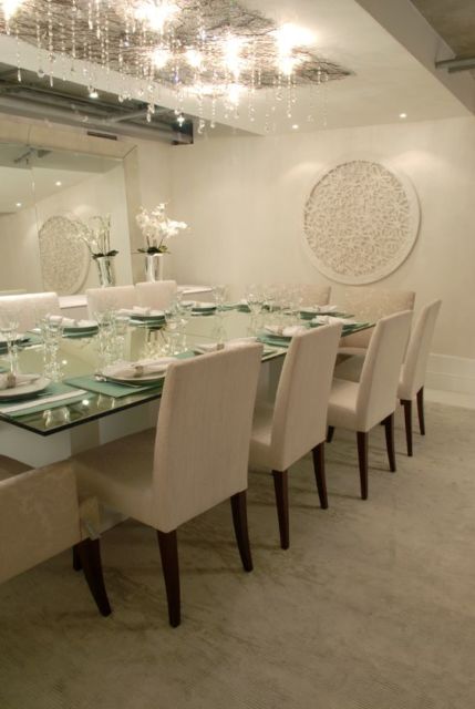 mesa de vidro com dez cadeiras, espeçho na parede frontal e lustre retangular cmprido com pendentes de critais