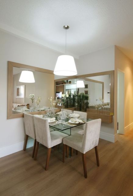 sala de jantar com mesa de vidro com 5 cadeiras brancas, dois grandes espelhos em ângulo reto e lustre branco