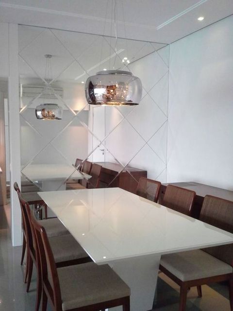 sala de jantar com mesa branca com seis cadeiras, espelho recortado em losangos e lustre cromado
